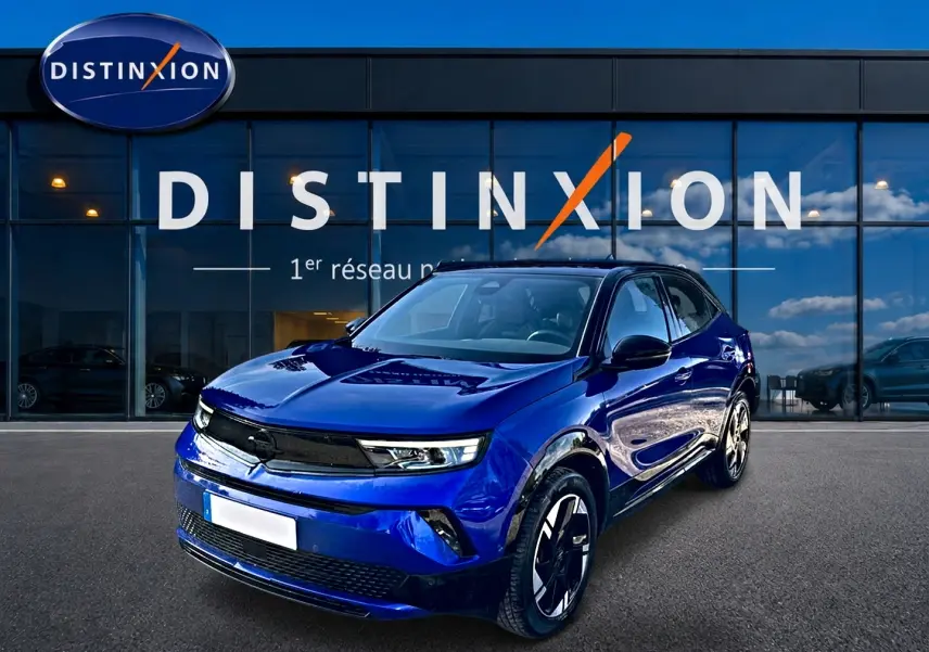 Opel Mokka Electric 156 gs bleu en 3/4 avant droit devant une vitrine avec logo Distinxion.
