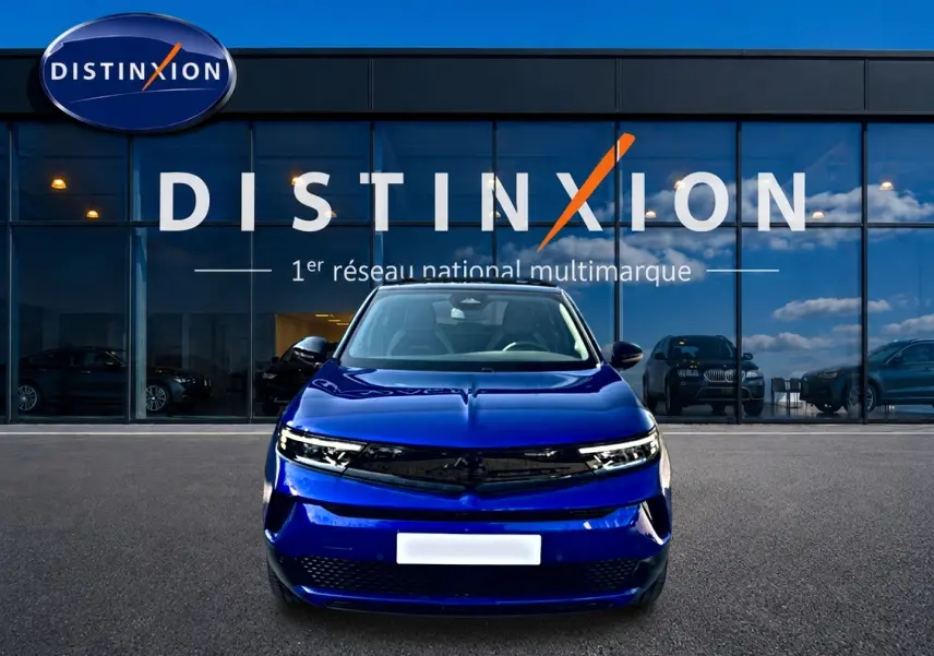 Opel Mokka Electric 156 GS bleu vue de face, avec calandre noire et phares LED fins, devant showroom Distinxion.