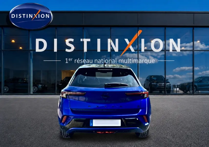 Vue arrière d'un Opel Mokka Electric 156 gs bleu, garé devant une vitrine avec logo Distinxion.