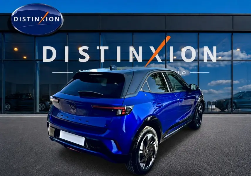 Vue 3/4 arrière droite d’un Opel Mokka Electric 156 gs bleu avec toit noir devant une vitrine Distinxion.