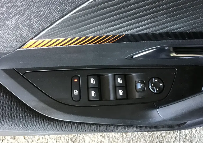 Détail du panneau de commandes des vitres et rétroviseurs côté gauche d’un Peugeot 2008 gris Artense avec insert décoratif carbone et orange.