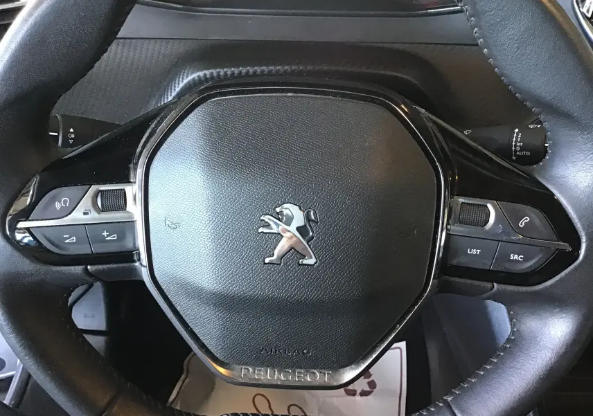 Gros plan sur le volant cuir noir du Peugeot 2008 1.5 BlueHDi 110, avec commandes intégrées et logo lion central.