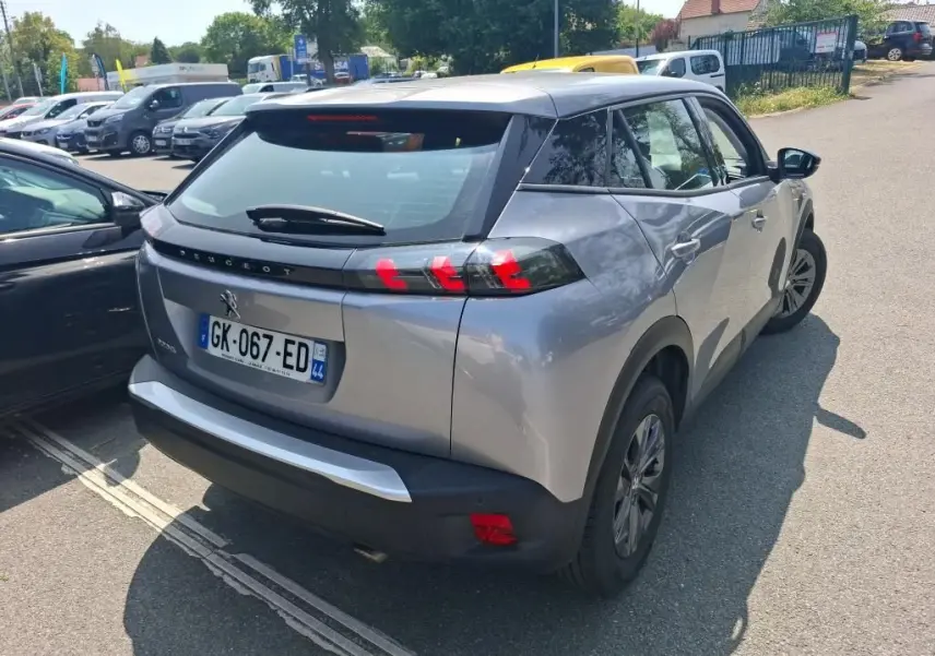 Peugeot 2008 gris Artense vue de profil côté gauche sur parking gravillonné avec protections noires sur les passages de roues.