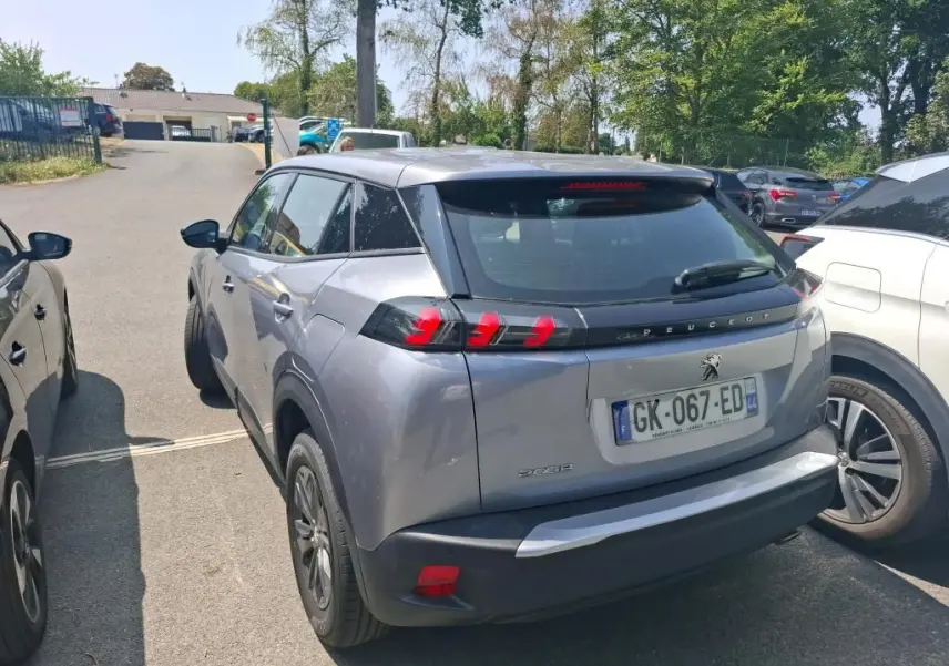 Peugeot 2008 gris Artense vue 3/4 arrière droit sur parking, avec toit noir et feux arrière distinctifs.