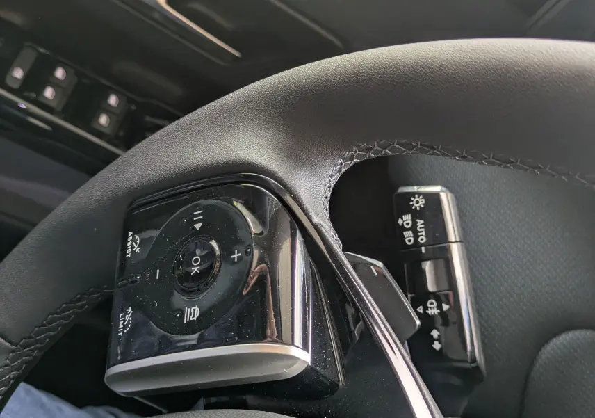 Gros plan sur les commandes au volant côté gauche du Citroën C5 Aircross hybride 2026, intérieur noir.