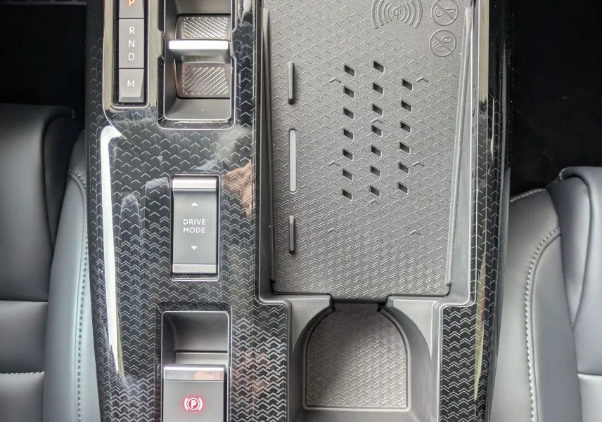 Vue plongeante sur la console centrale noire brillante du Citroën C5 Aircross hybride 2026 avec commandes de boîte auto et zone de recharge sans fil.