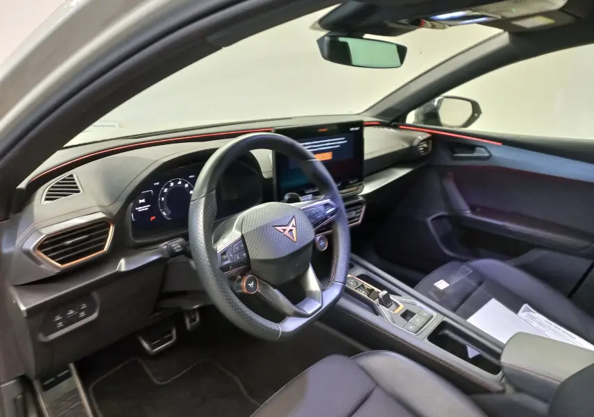 Vue intérieure côté conducteur du CUPRA LEON ST 1.5 eTSI 2025, avec éclairage d'ambiance rouge et tableau de bord digital.