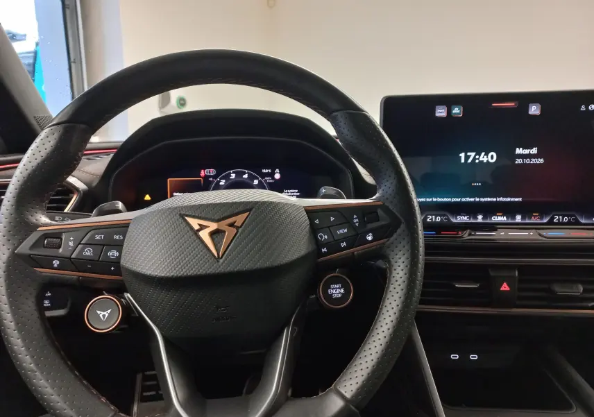 Vue intérieure centrée sur le volant perforé noir avec logo cuivré CUPRA et écran digital du tableau de bord.