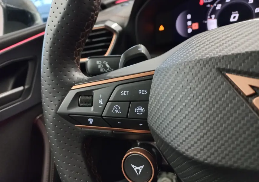Gros plan sur le volant perforé gris carbone du CUPRA LEON ST 1.5 eTSI avec commandes de régulateur et logo cuivré.