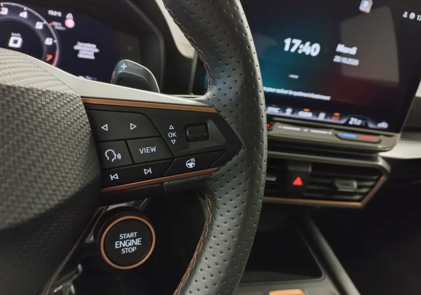 Vue rapprochée du volant perforé avec commandes et bouton start/stop, tableau de bord numérique et écran central du CUPRA LEON ST gris Taiga.