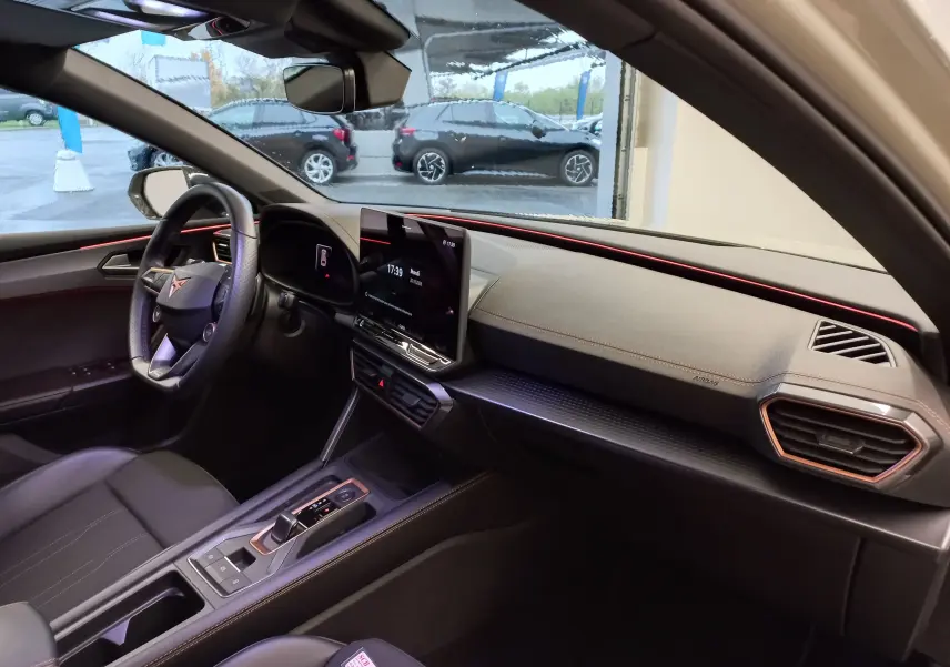 Intérieur de la CUPRA LEON ST 1.5 eTSI 2025 vu côté conducteur, avec tableau de bord gris et éclairage d’ambiance rouge.