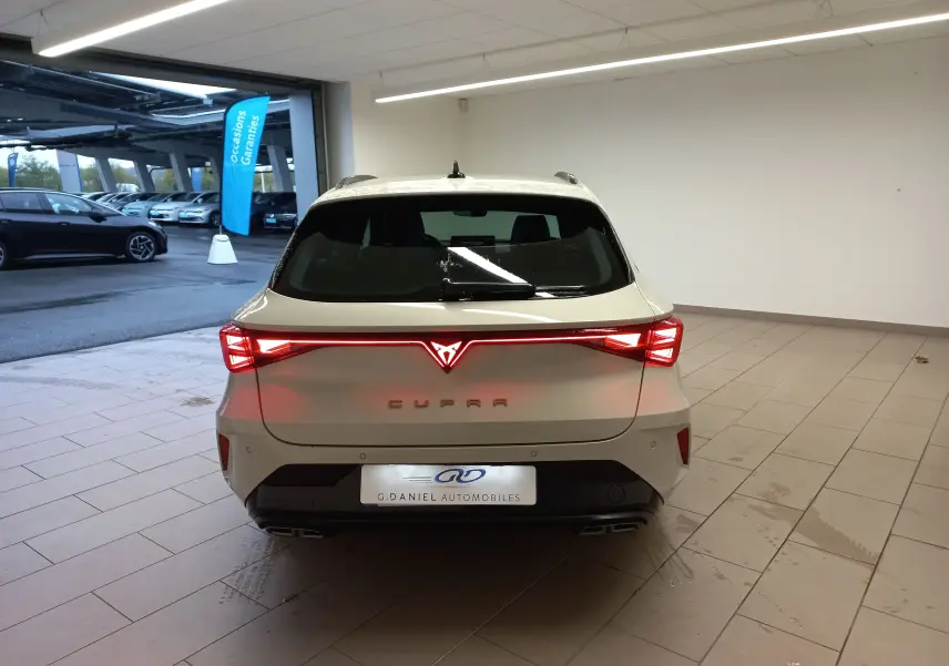 Vue arrière d'une CUPRA Leon ST 1.5 eTSI 150 DSG7 en gris Taiga avec feux arrière allumés dans un garage.