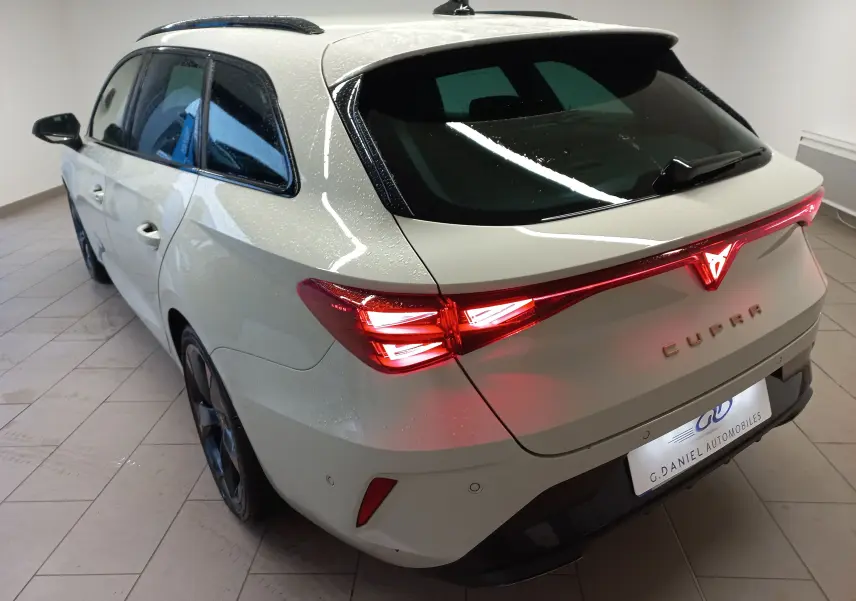 Vue 3/4 arrière droite d'une CUPRA LEON ST 1.5 eTSI 150 DSG7 en gris Taiga avec feux arrière allumés et jantes cuivrées.