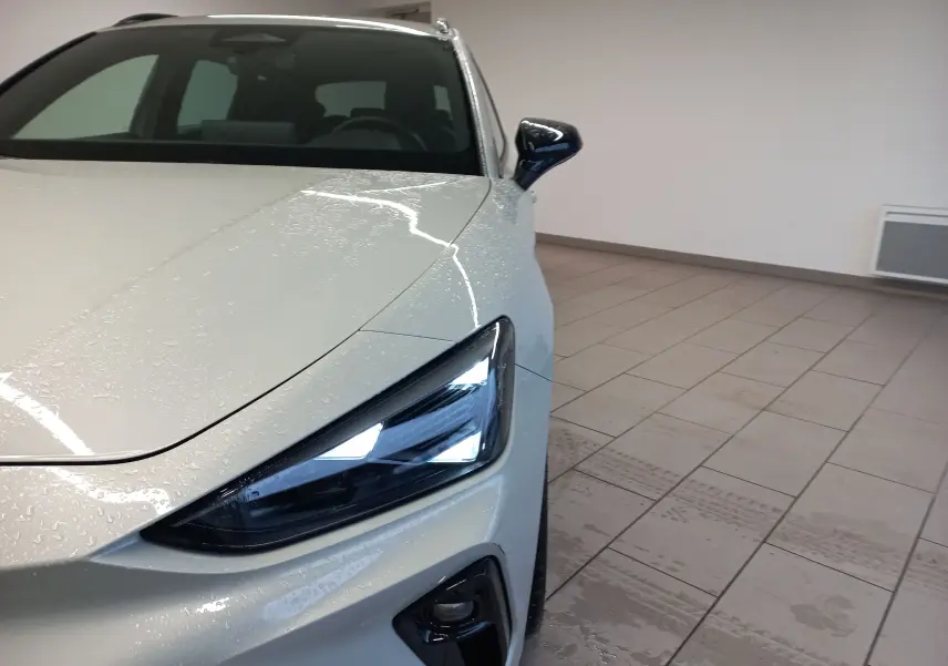 Gros plan sur l'avant droit gris Taiga du CUPRA LEON ST 1.5 eTSI 150 DSG7 avec phares LED allumés en intérieur.