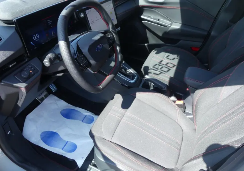 Intérieur Ford Puma 2025 vu côté conducteur, sièges tissu gris avec surpiqûres rouges et volant multifonction.