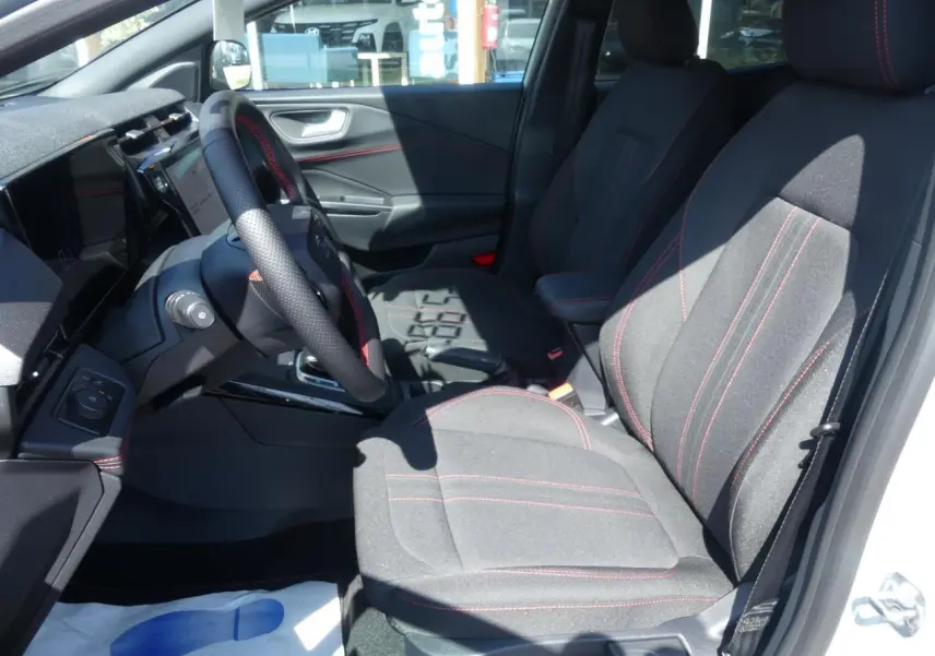Intérieur avant droit du Ford Puma 2025, sièges tissu gris avec surpiqûres rouges et volant sport perforé.