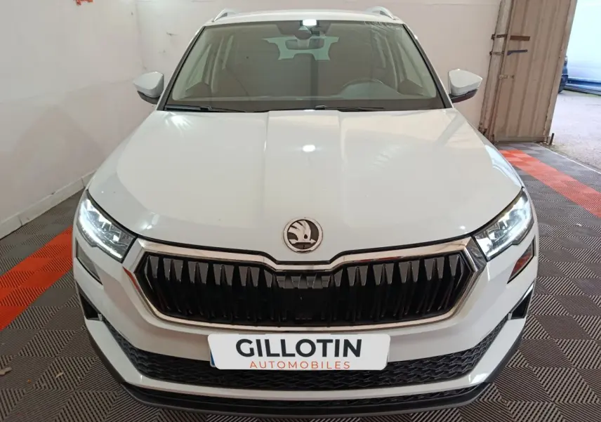 Vue avant d'un Skoda Karoq blanc avec calandre noire et phares LED allumés en intérieur showroom.