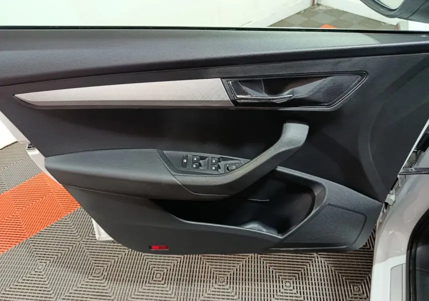 Gros plan sur la porte avant gauche noire du Skoda Karoq 2024 avec commande des vitres et poignée intégrée.