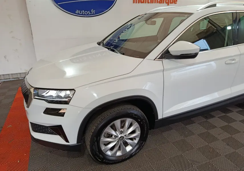 Vue 3/4 avant droit d'un Skoda Karoq blanc avec jantes alliage et phares LED dans un showroom.