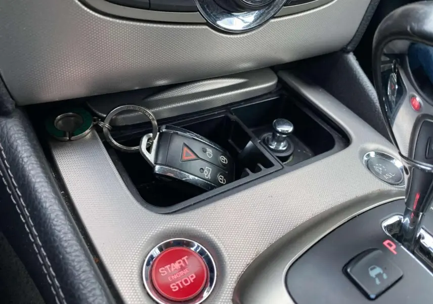 Gros plan sur la console centrale gris clair du Jaguar XK 2009 avec bouton start/stop rouge et clé dans le rangement.