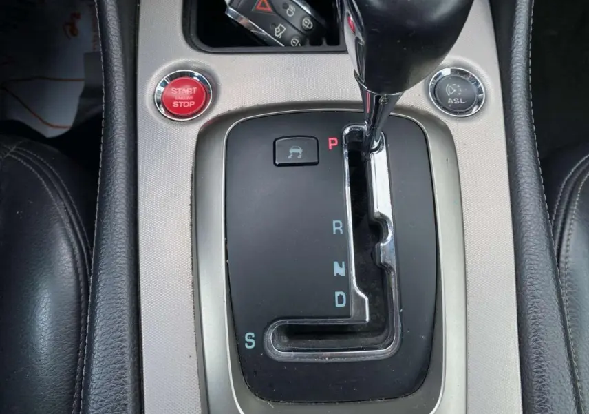 Gros plan sur la console centrale de la Jaguar XK 2009, levier de boîte auto et bouton rouge Start/Stop visibles.