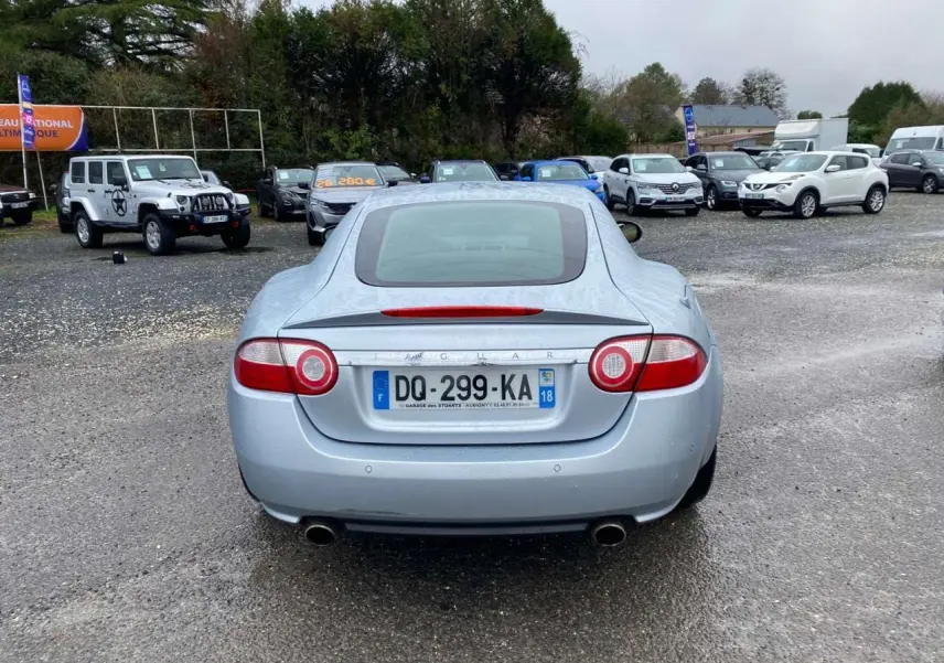 Vue arrière d'une Jaguar XK Coupé gris clair de 2009 avec feux ronds et double sortie d'échappement visible.