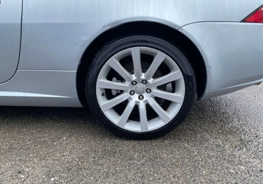 Gros plan sur la roue arrière droite gris clair d'une Jaguar XK Coupé 4.2i V8 de 2009 sous la pluie.