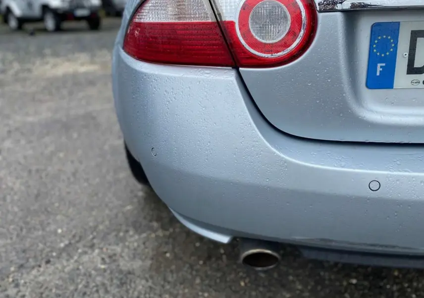 Gros plan sur l'arrière droit gris clair d'une Jaguar XK 4.2i V8 2009 avec feu rond et sortie d'échappement visible.