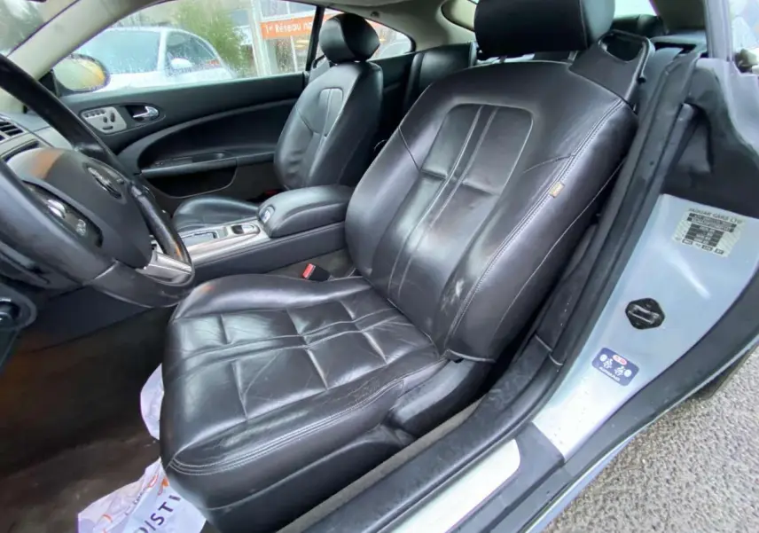 Vue intérieure côté conducteur de la Jaguar XK Coupé gris clair 2009, sièges en cuir noir et console centrale visible.