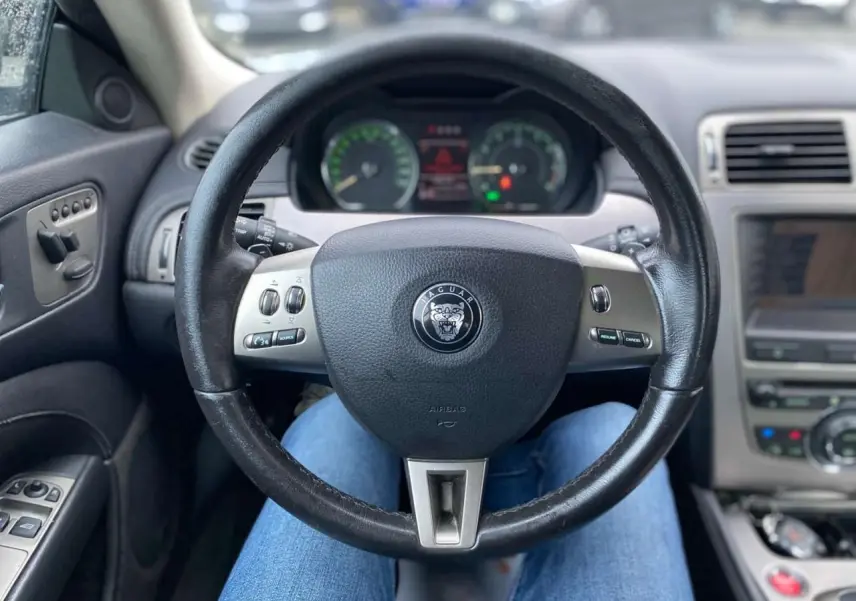 Vue intérieure centrée sur le volant noir de la Jaguar XK 4.2i V8 2009 avec commandes intégrées et tableau de bord flou.