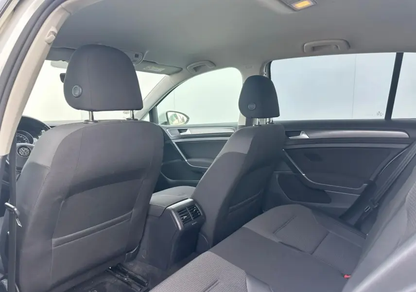 Vue intérieure arrière côté gauche de la Volkswagen Golf VII blanche, montrant les sièges en tissu noir et les aérateurs centraux.