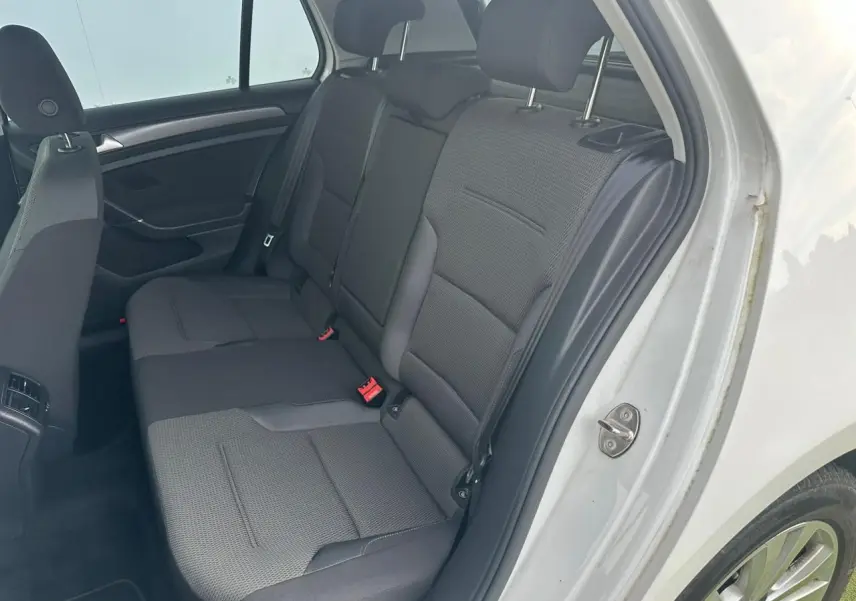 Vue côté droit de la banquette arrière grise de la Volkswagen Golf VII blanche avec appuie-têtes et ceintures de sécurité.