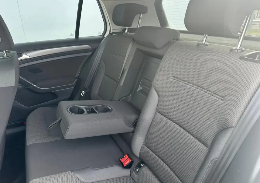 Vue intérieure côté droit de la banquette arrière grise avec accoudoir central relevé et porte-gobelets d'une Volkswagen Golf VII blanche.