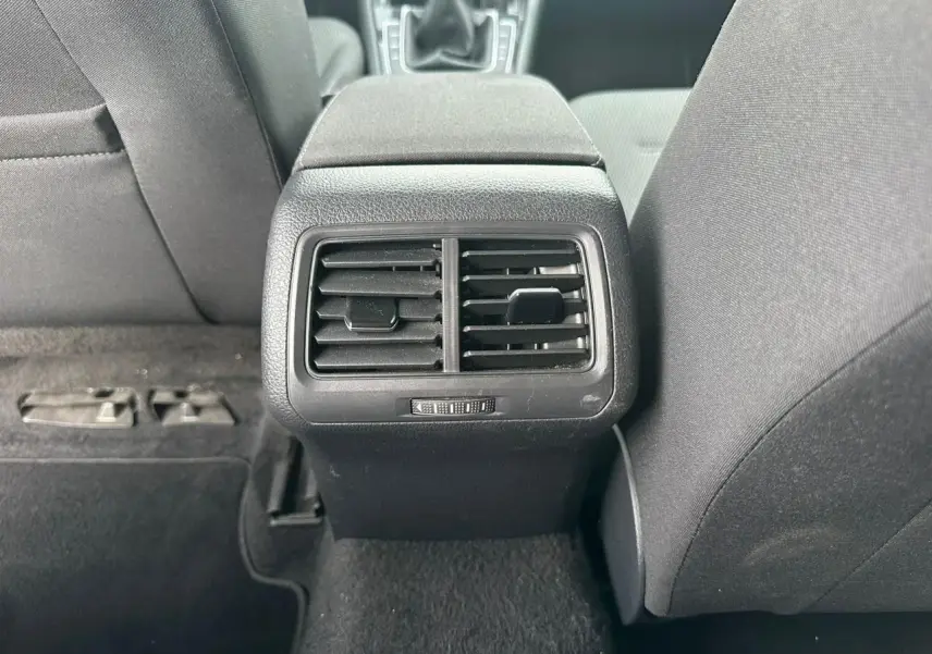 Gros plan sur les bouches d'aération arrière noires entre les sièges avant gris foncé d'une Volkswagen Golf VII blanche.