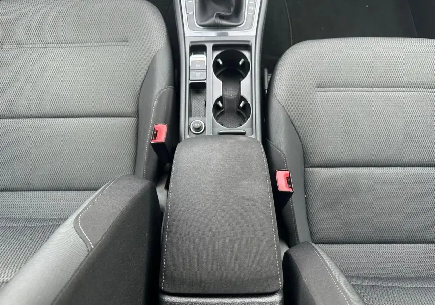 Vue plongeante sur l'accoudoir central noir et les sièges avant en tissu gris de la Volkswagen Golf VII blanche.