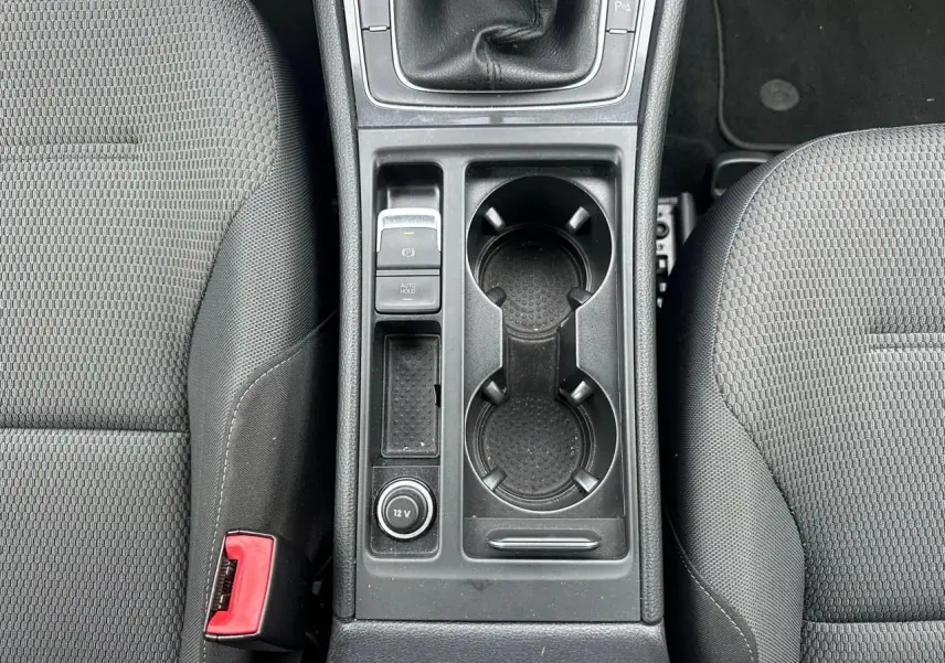 Vue plongeante sur la console centrale noire de la Volkswagen Golf VII blanche, avec porte-gobelets et levier de vitesses manuel.