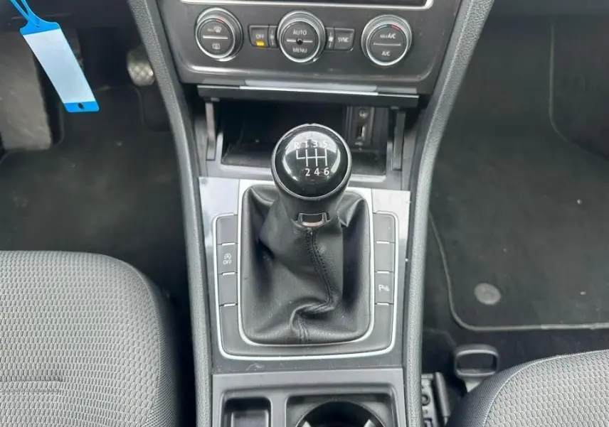 Vue rapprochée de la console centrale noire avec levier de vitesses manuel et sièges tissu gris d'une Volkswagen Golf blanche.