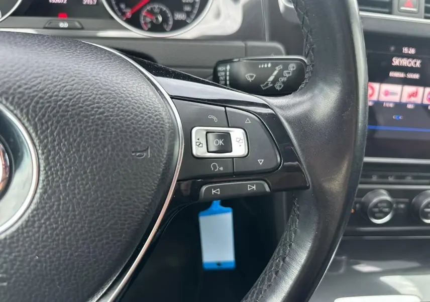 Gros plan sur le volant cuir côté gauche de la Volkswagen Golf blanche avec commandes multifonctions et tableau de bord visible.
