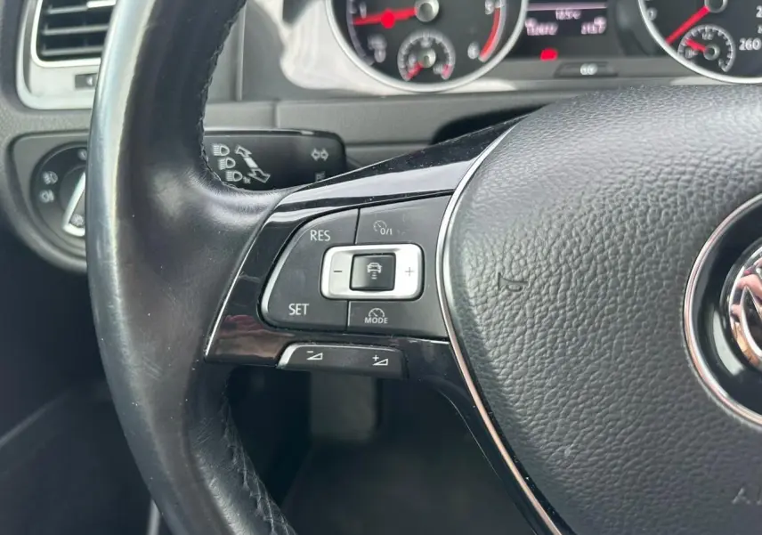 Gros plan sur le volant multifonction en cuir noir d'une Volkswagen Golf VII 2018, avec commandes de régulateur de vitesse.
