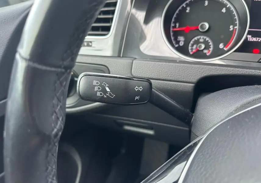 Gros plan sur la manette de clignotant à gauche du volant noir, avec tableau de bord et compte-tours visibles.