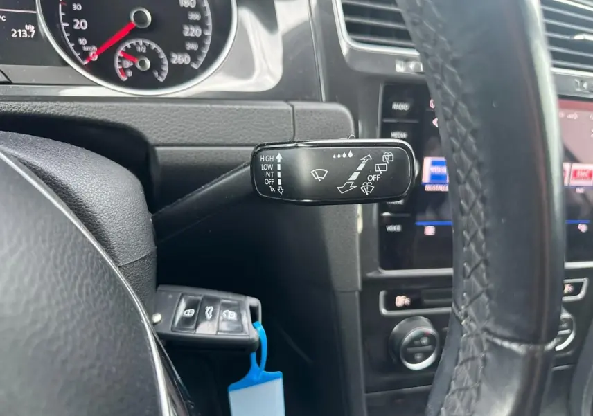 Gros plan sur le commodo d’essuie-glace à gauche du volant en cuir d’une Volkswagen Golf blanche, tableau de bord visible.