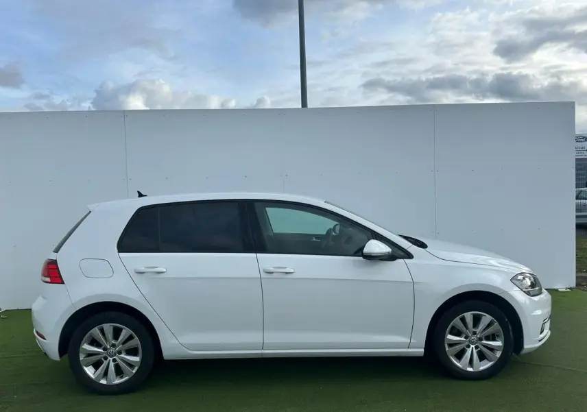 Vue de profil côté gauche d'une Volkswagen Golf VII blanche sur fond neutre extérieur.
