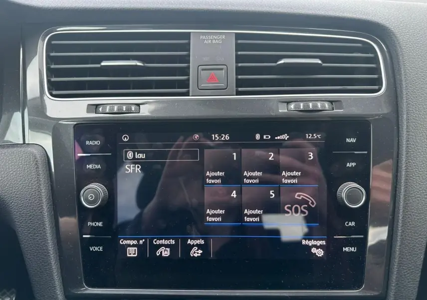 Vue rapprochée de l'écran tactile central noir du système multimédia d'une Volkswagen Golf blanche, avec commandes autour.