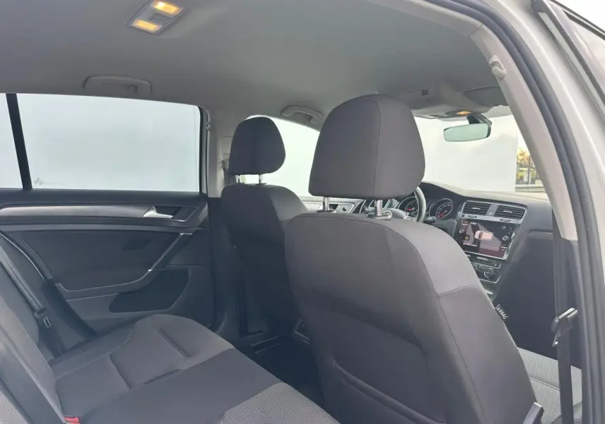 Vue intérieure arrière côté gauche de la Volkswagen Golf VII blanche, montrant les sièges en tissu noir et le tableau de bord avant.
