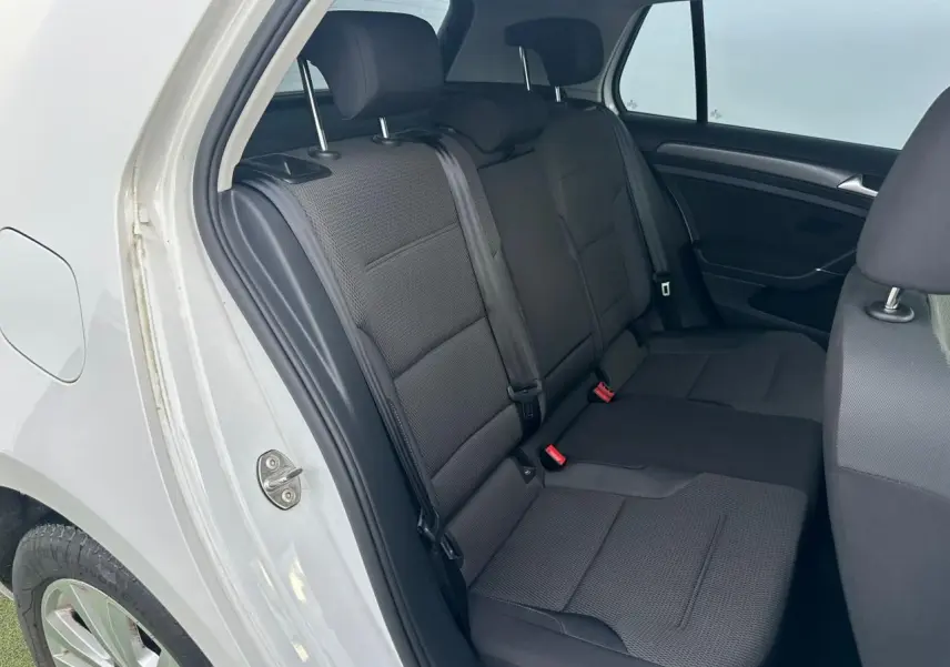Vue intérieure côté arrière droit montrant la banquette noire et les ceintures de sécurité d'une Volkswagen Golf blanche.