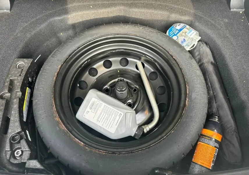 Vue plongeante sur la roue de secours noire dans le coffre d'une Volkswagen Golf blanche avec kit de réparation pneus.