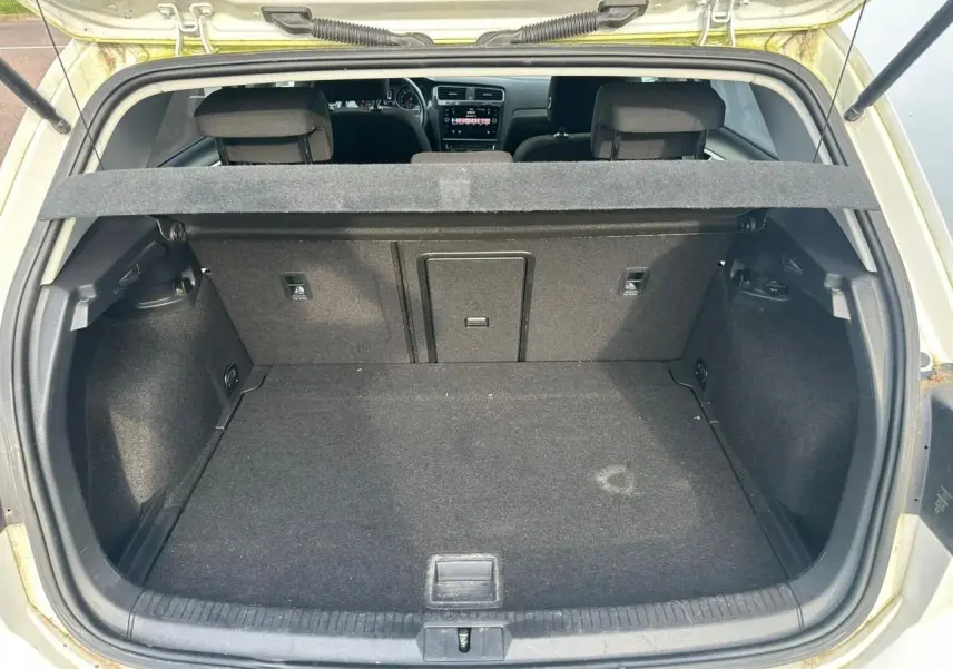 Coffre ouvert vu de l'arrière d'une Volkswagen Golf blanche, avec banquette arrière et tablette cache-bagages visibles.