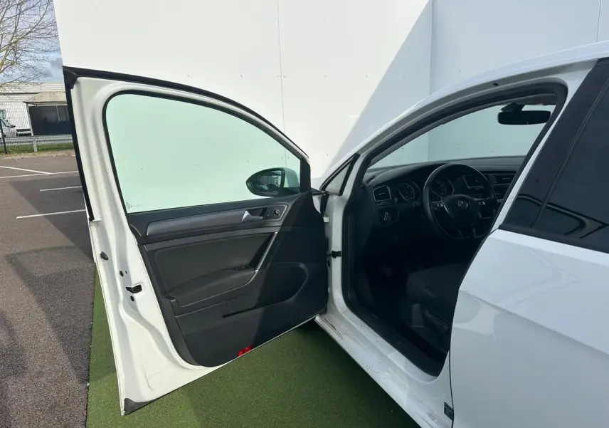 Vue côté gauche avant d'une Volkswagen Golf blanche 2018 avec porte ouverte dévoilant l'intérieur noir et le volant multifonction.