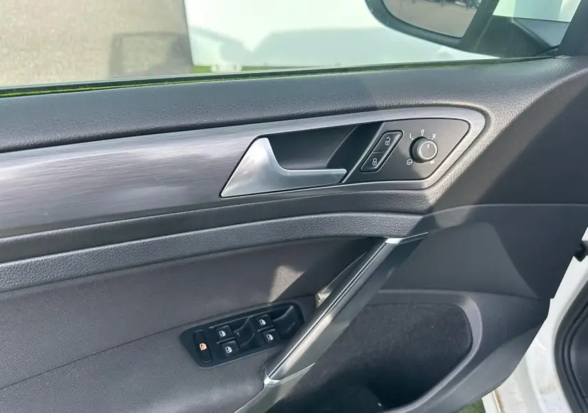 Vue intérieure côté gauche de la porte avant d’une Volkswagen Golf blanche, avec commandes de vitres et rétroviseurs.