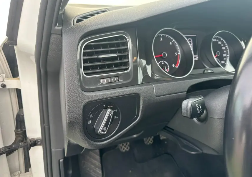 Vue intérieure côté gauche du tableau de bord noir d'une Volkswagen Golf blanche avec commandes d'éclairage et compteurs.